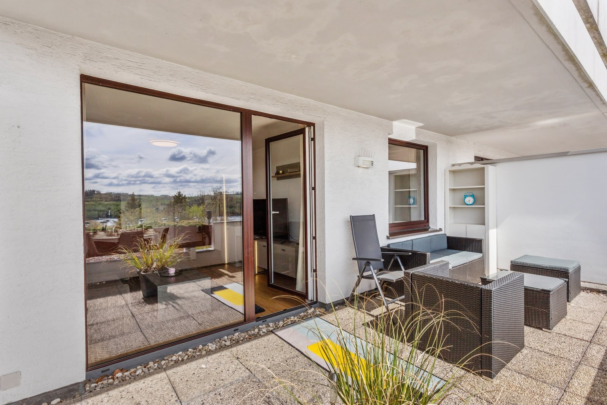 A balcony with a view of a lake, outdoor furniture, and a sliding glass door leading to an interior space.