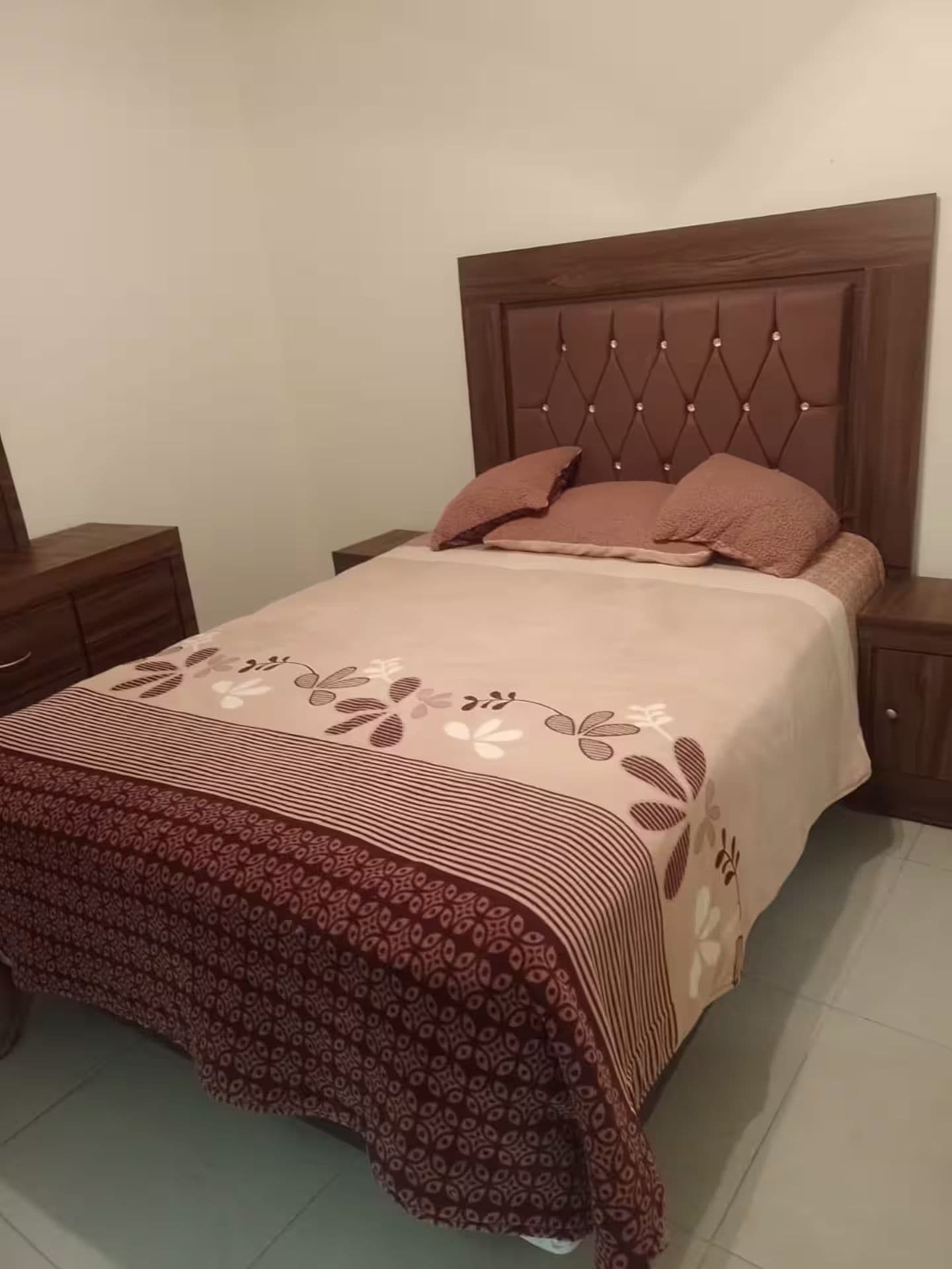 A bed with a patterned bedspread, a tufted headboard, and two bedside tables.