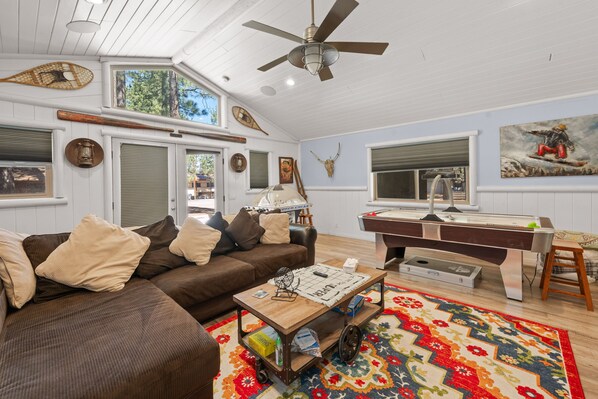 Bright game room featuring sectional sofa seating, coffee table, air hockey table, dome hockey, vaulted white ceilings, and decorative snowshoes and paddles. - Big Bear Hot Tub | Game Room + Putting Green (Big Bear Lake)