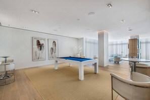 A modern living room with a pool table, a dining area, and a large window. - 5-Star Luxury Condo at Tiffany House -7th floor (Fort Lauderdale)
