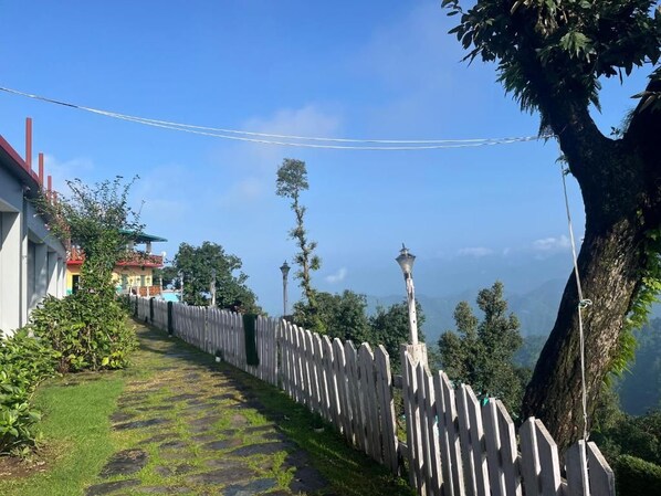 A pathway with a white fence, a tree, and a building with a red roof.