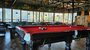 A pool table with balls, surrounded by seating and a view of greenery. - Shiva Valley Resort (Dhanaulti)