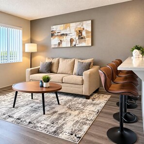 Ein stilvolles Wohnzimmer mit Sofa, Couchtisch, Teppich und einer Bar mit Hockern.