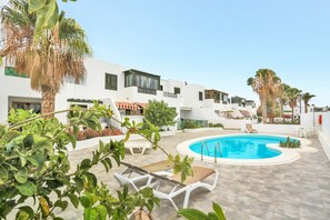 A pool area with lounge chairs, a clear blue pool, and white buildings with balconies. - Apartamento NATALIA BEACH (Puerto del Carmen)