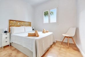 A bedroom with a bed, a nightstand, a chair, and a window with a view of palm trees. - Apartamento NATALIA BEACH (Puerto del Carmen)