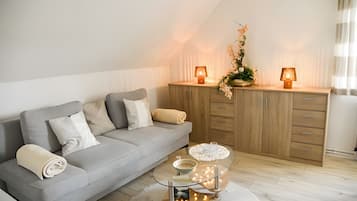 A modern living room with a grey sofa, two lamps, a decorative glass table, and a wooden cabinet.