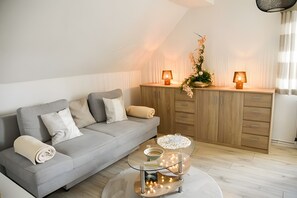 Una sala de estar moderna con un sofá gris, dos lámparas, una mesa de vidrio decorativa y un aparador de madera.