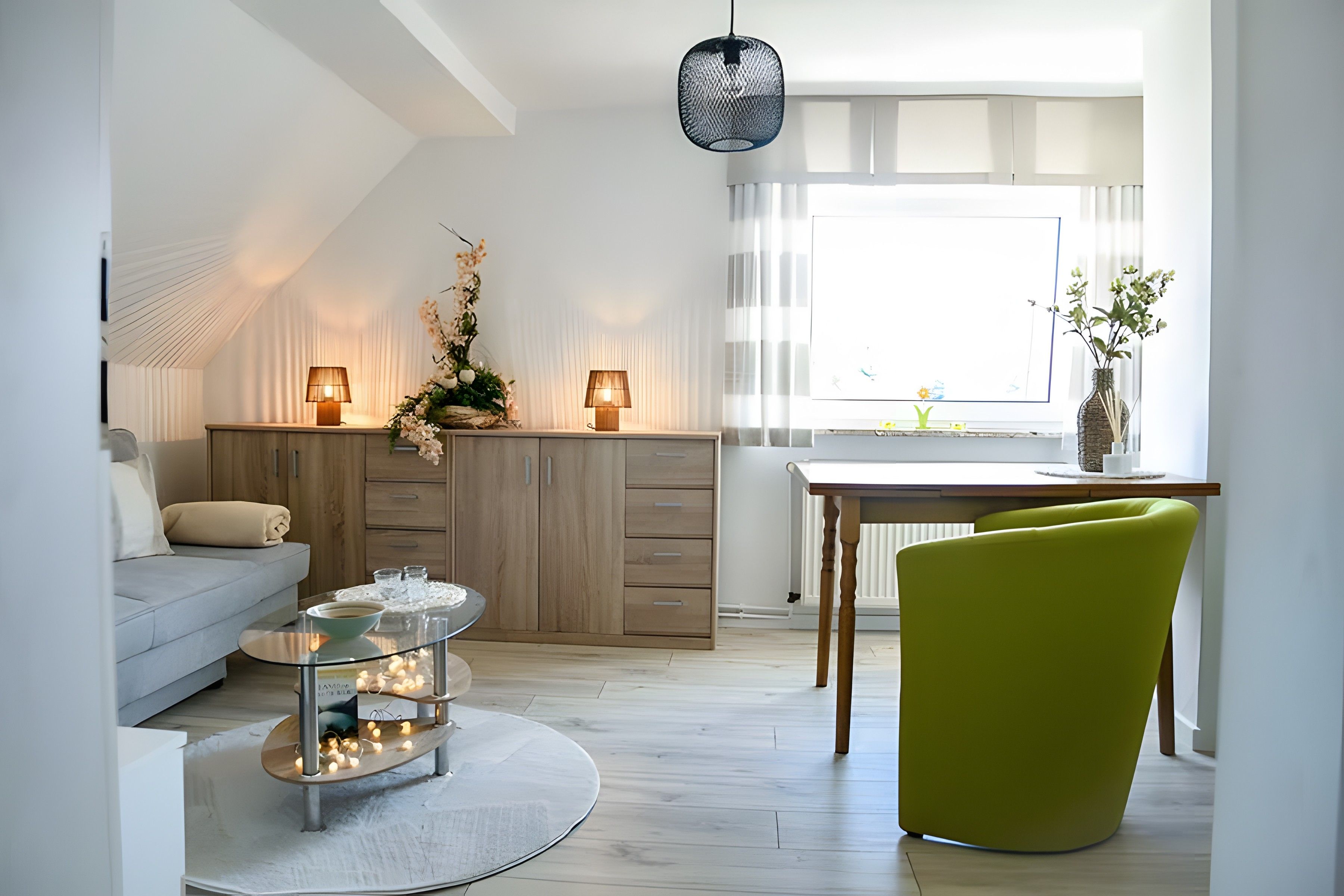 Un salon moderne avec un canapé, une table à manger et un fauteuil vert. Il y a deux lampes sur la table et un luminaire suspendu au plafond.