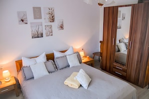 A neatly made bed with pillows and a folded towel, a bedside table with a lamp, and a wooden wardrobe.
