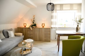 A modern living room with a sofa, a dining table, and chairs. There is a decorative plant on the table and a hanging light fixture above.