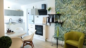 A modern kitchen with white cabinetry, a dining area with a round table and chairs, and a green leafy wallpaper.