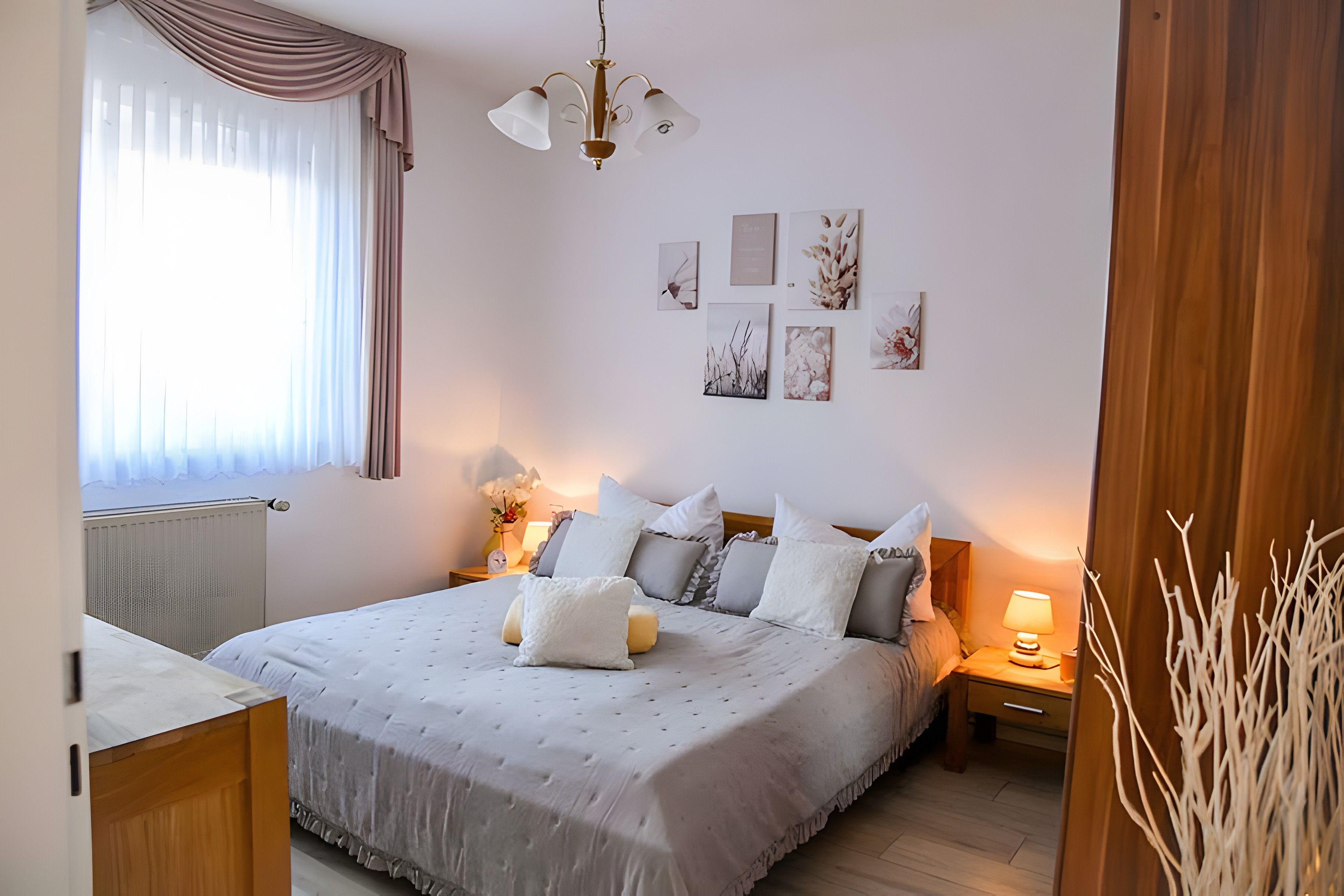 A bedroom with a bed, bedside tables, a lamp, a radiator, and artwork on the wall.