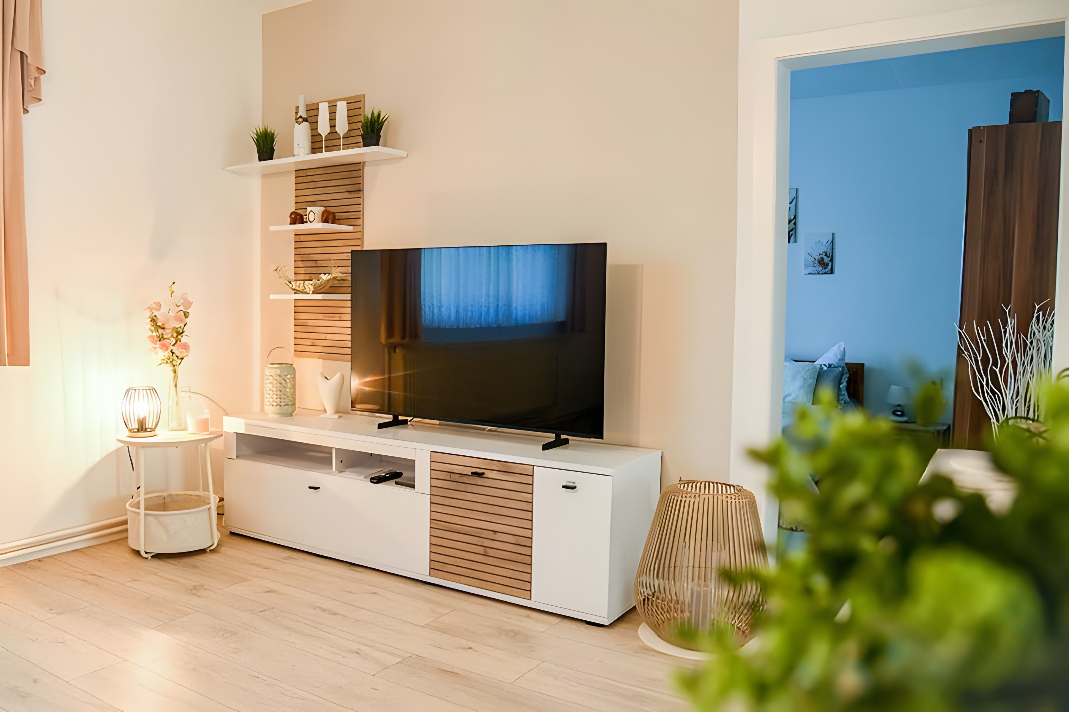Ein modernes Wohnzimmer mit einem Flachbildfernseher, Holzböden, einem kleinen Tisch mit einer Vase und einer Topfpflanze.