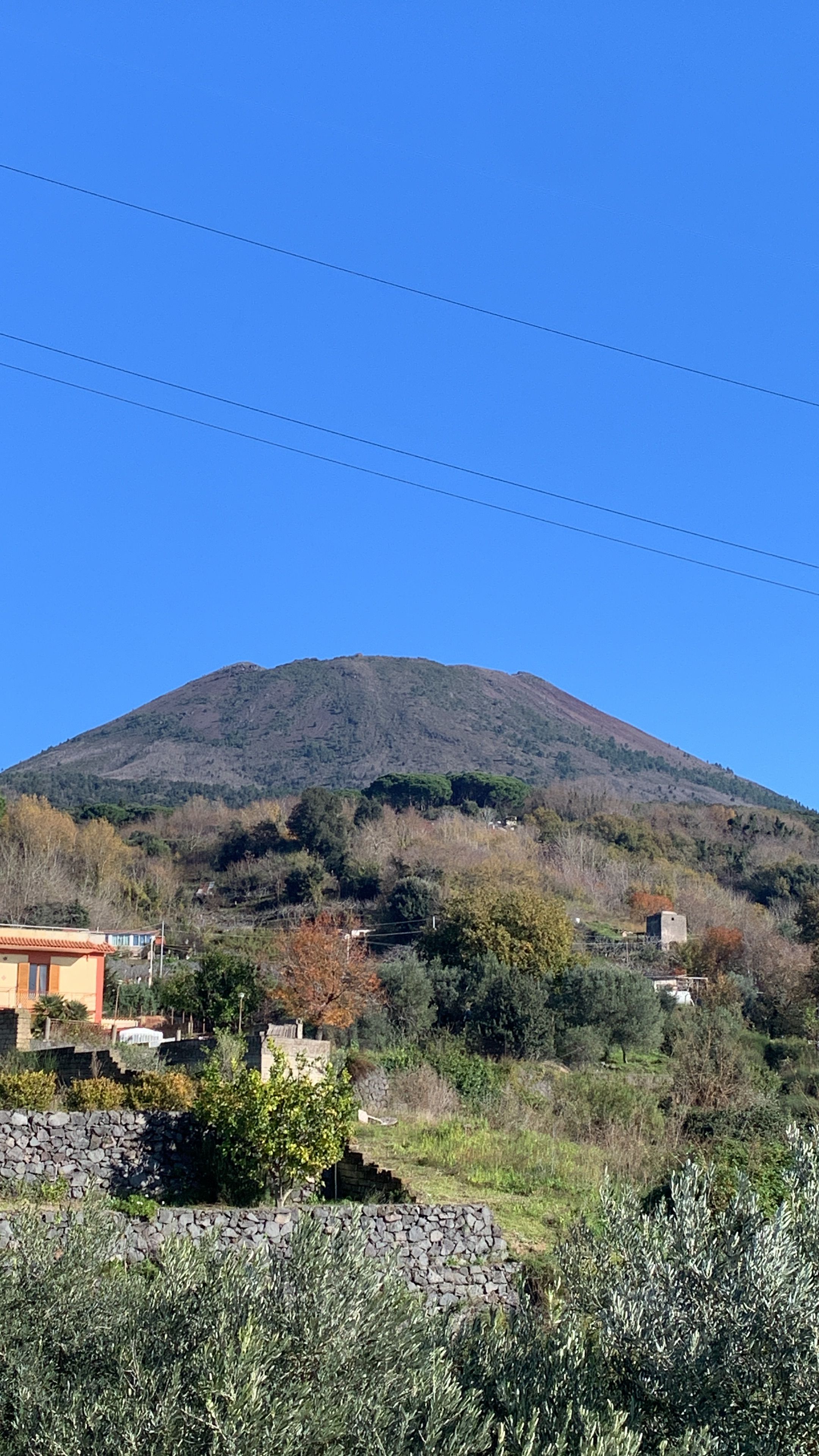 Una muntanya sota un cel clar, envoltada de vegetació i alguns edificis.
