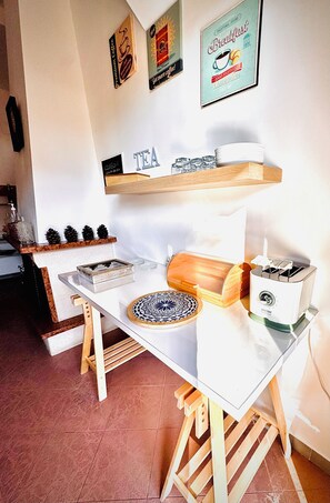A kitchen with a white countertop, a coffee machine, a tea kettle, and a toaster. There are pine cones and a decorative plate on the counter.
