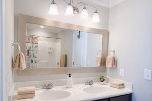 Une salle de bain avec deux lavabos, un grand miroir et trois luminaires au plafond.