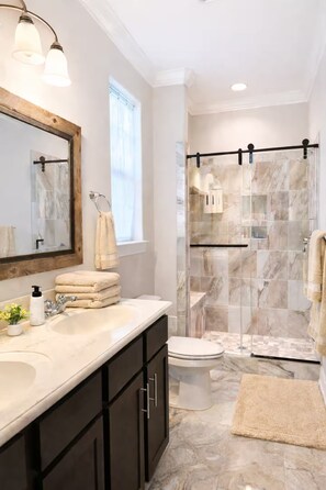 A modern bathroom with a double sink vanity, a large mirror, a glass shower enclosure, and a marble-tiled shower area. - Family-Friendly 4BR • Beach Access • Backyard (Myrtle Beach)