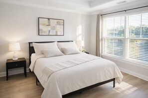 Een slaapkamer met een bed, twee nachtkastjes, een kunstwerk aan de muur en een groot raam met zonwering.