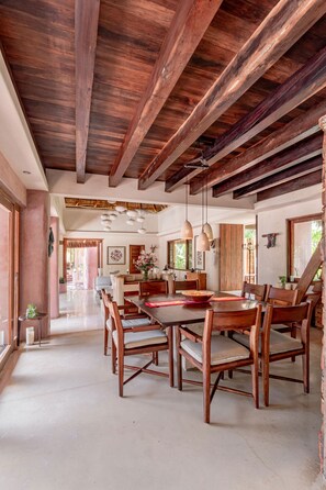 A spacious dining area with wooden tables and chairs, a high ceiling with exposed beams, and a view of a lush garden through the windows. - Casa Cantarena—Private Beach, 4 Bedrooms, 4 Bathrooms, Chef + Concierge (Quintana Roo)