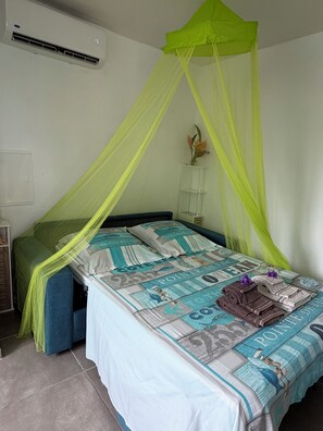 A bedroom with a bed covered in a patterned bedspread, a green canopy, and a bedside table with a vase of flowers. - Ground-floor studio in a rural setting overlooking the sea (Le François)