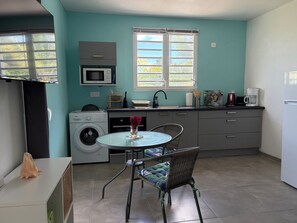 A compact kitchen with a microwave, washing machine, and a dining area with a table and chair. - Ground-floor studio in a rural setting overlooking the sea (Le François)