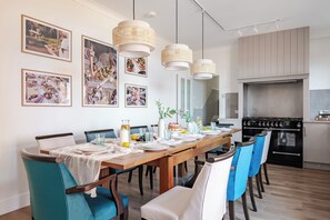 A dining area with a long wooden table set for a meal, surrounded by chairs with blue and white upholstery. - Cromer Coastal Escape | 2 Mins to Beach, Pool Table & Games Room | Sleeps 11 (Cromer)