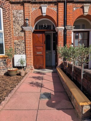 A brick building with a large wooden door marked with the number 13, a stone wall, and potted plants along the walkway. - Cromer Coastal Escape | 2 Mins to Beach, Pool Table & Games Room | Sleeps 11 (Cromer)
