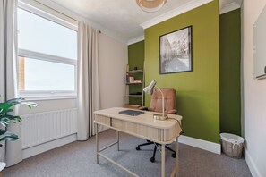 A room with a desk, chair, radiator, bookshelf, and a window with curtains. - Cromer Coastal Escape | 2 Mins to Beach, Pool Table & Games Room | Sleeps 11 (Cromer)