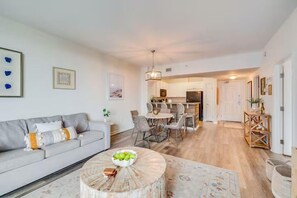 A modern living room with a sofa, dining table, and chairs, leading to a kitchen area with a dining table and chairs. - ☀️Palms 1809 | Beautiful Views | Beach Nearby | Lagoon Pool🌴 (Destin)