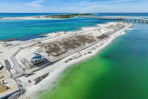 An aerial view of a coastal area with a pier extending into the water, a sandy beach, and a building with a blue roof near the shore. - ☀️Palms 1809 | Beautiful Views | Beach Nearby | Lagoon Pool🌴 (Destin)