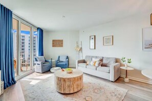 A modern living room with a sofa, two armchairs, a coffee table, and a view through large windows. - ☀️Palms 1809 | Beautiful Views | Beach Nearby | Lagoon Pool🌴 (Destin)