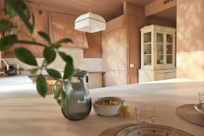 A dining area with a table set for two, a pitcher, a bowl of fruit, and a cabinet in the background.