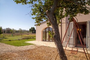 A building with a large arched doorway, a swing set, and a clear view of the surrounding landscape. - Casa Montessori Brughiera - A Haven for Little Dreamers (Jesi)