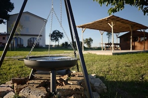 A barbecue grill set up on a stone base outdoors with a wooden structure in the background.
