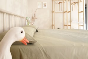 A bed with a green bedspread, a white pillow, and a white swan head in the foreground.