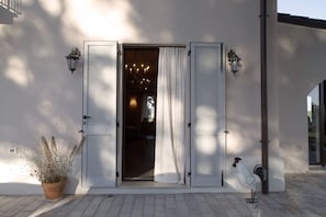 A building entrance with a door, a potted plant, and a rooster statue.