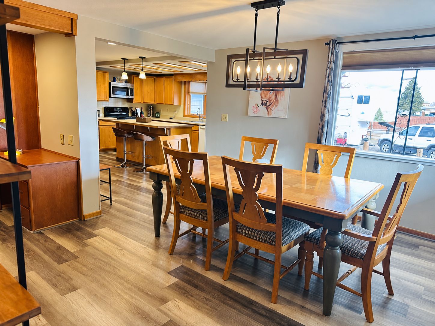 A modern kitchen with wooden cabinets, a central island, and a dining area with a wooden table and chairs.