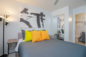 A modern bedroom with a large bed, a nightstand, a floor lamp, and a bathroom visible through an open door. - ⭐Across St from Beach Access-Gulf Views-Pool+Hot Tub-Summer Breeze 310⭐ (Miramar Beach)