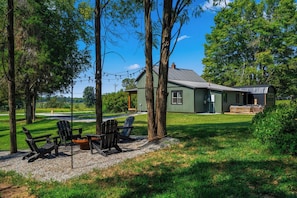 A green house with a deck, surrounded by trees and a gravel area with Adirondack chairs. - Lake Cumberland Farmhouse: Arcade Room, Fire Pit, Boat Parking, Pet Friendly (Russell Springs)