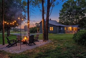 A cozy outdoor seating area with a fire pit, surrounded by trees and string lights. - Lake Cumberland Farmhouse: Arcade Room, Fire Pit, Boat Parking, Pet Friendly (Russell Springs)
