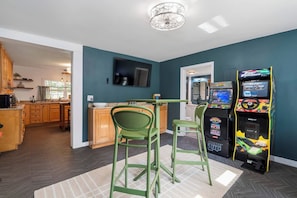 A modern kitchen with a dining area, arcade games, and a TV. - Lake Cumberland Farmhouse: Arcade Room, Fire Pit, Boat Parking, Pet Friendly (Russell Springs)