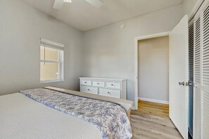 Ein Schlafzimmer mit Bett, Kommode, Fenster und Tür.