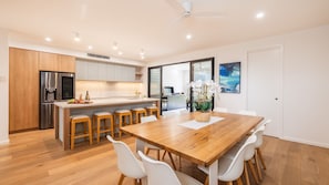 A modern kitchen with a central island, wooden flooring, and a dining area with a wooden table and white chairs. - Gloucester Escape, 37a Gloucester St - stunning duplex with fabulous water views (Nelson Bay)