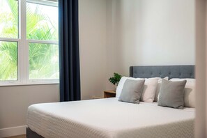 Une chambre à coucher avec un lit, une table de chevet, une plante en pot et une fenêtre avec des rideaux.