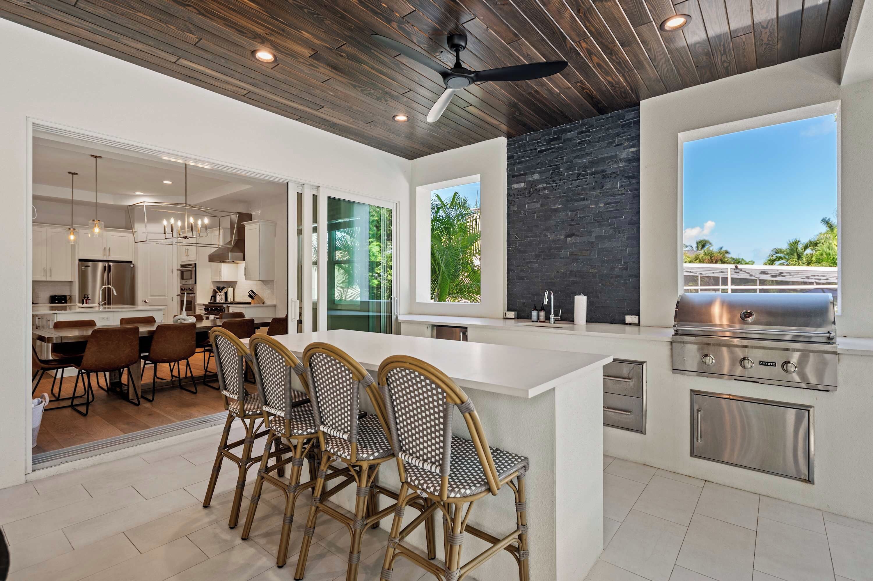 Una cocina moderna con una isla central, comedor con sillas de mimbre y vistas al exterior.
