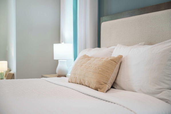 Un lit bien fait, avec du linge de lit blanc et un coussin beige à texture intéressante.