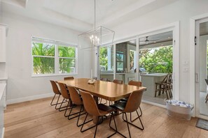 Un espace de repas moderne avec une table et des chaises en bois, de grandes fenêtres et une vue sur l’extérieur.