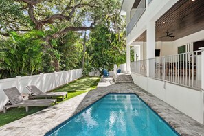 Une piscine entourée d’une clôture blanche, avec des chaises longues et un escalier menant à un espace abrité.