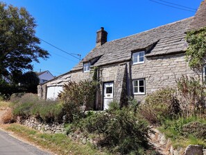 A stone cottage with a sloped roof, a chimney, and a small window. - Farthing Cottage (Wareham)