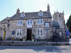 A stone building with a sign for 'The Old Curiosity Shop' and a directional sign for Castle St. - Farthing Cottage (Wareham)